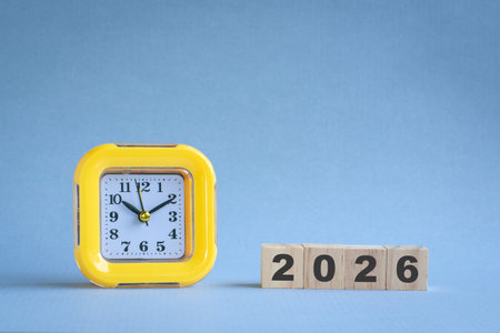 2026 on wooden blocks next to yellow table clock. New year concept.の写真素材