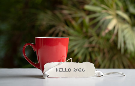 Hello 2026 on a piece of torn white paper, next to red coffee cup and ear phones.の写真素材