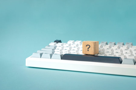 Question mark on wood block on top of keyboard. Isolated on light blue background.