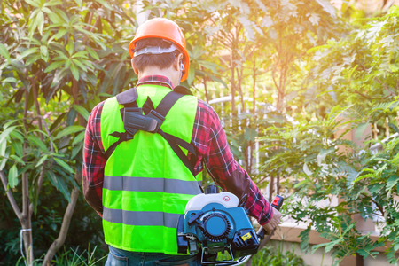 workman holding lawn mower machine cutting grass in garden on morning