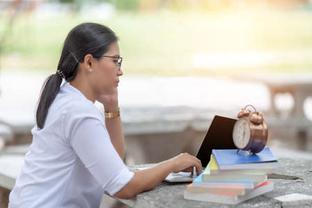 Portrait of female student sitting at the park and using laptop ,  writing thesis with serious face expression. Young asian woman working on her home assignmentの写真素材