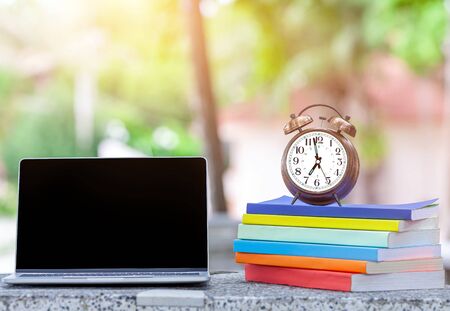 close up of blank laptop on desk with pink alarm clock placed on the books.の写真素材