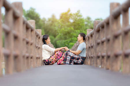 Couples sitting on wooden rustic bridge, spring scene,  with  hat enjoying the day in a parkの写真素材