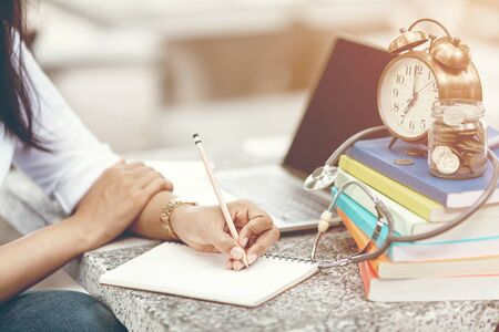 Close up of woman's hands writing in spiral notepad placed on desktop with various items