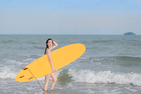 attractive sexy young asian woman surfer girl in bikini   poses on sandy beach with surfboard , water sports, healthy active lifestyle, summer vacation, extreme sport.の写真素材