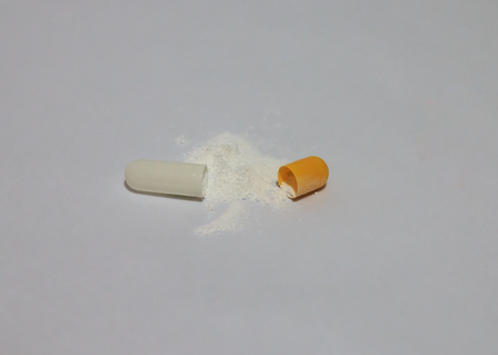 close up of open capsule and powder on white background