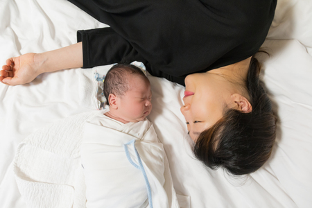 Asian young mother and her newborn baby sleeping peacefully on her bed in the bedroom.の写真素材