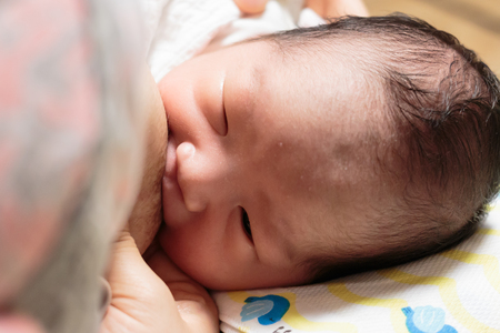 Asian baby is sucking at his mother's breast.の写真素材