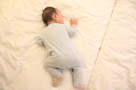 Asian little baby falling asleep on the bed in hotell roomの写真素材