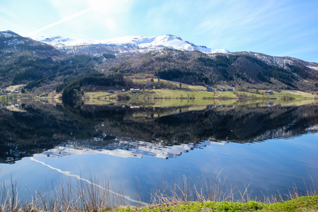 Calm and peaceful landscape in Norway. White capped mountain reflected in crystal clear lake.