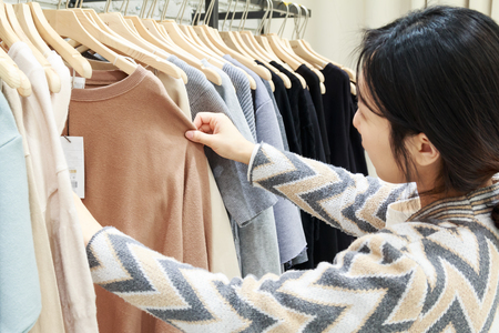 shopping concept - Asian woman choosing clothes at clothing shopの写真素材