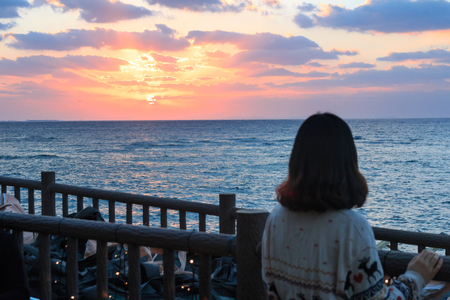 Asian young woman watching beautiful sunset over horizon on the waterfrontの写真素材