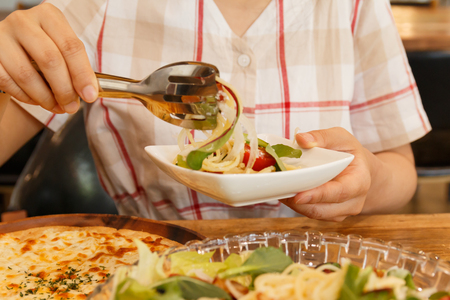 woman putting noodles into the dish on her handの写真素材