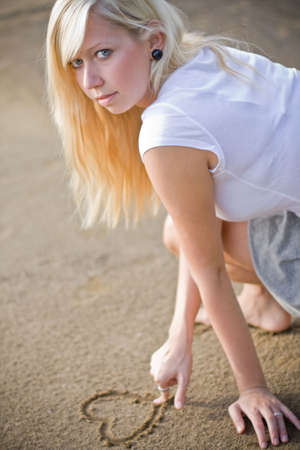 blond woman drawing a heart on the beach to show the loveの写真素材