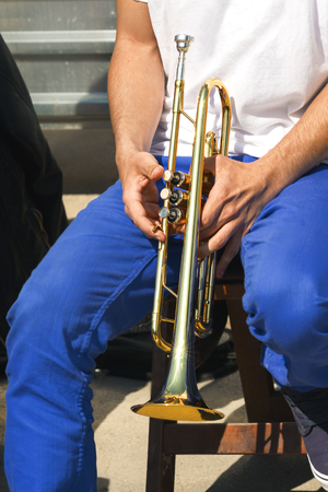 Male musician with white shirt and blue jeans sitting and holding trumpet.の写真素材