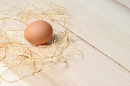 Organic speckled brown hen egg on wooden table with straw.の写真素材