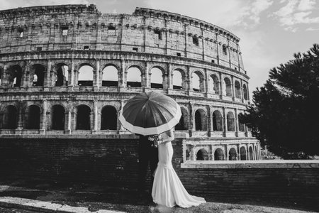Bride and groom kissing behind an Umbrella black and white in front of the Colosseum Rome, Italy.の写真素材