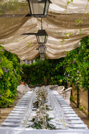 Outdoor Wedding dinner set up under a white pergola surrounded by green and lilac wisteria and white linens Villa Le Fontanelle Florence, Tuscany.の写真素材