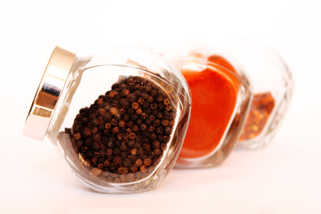 Three glass jars filled with spices isolated on white background. Black pepper in the foreground.の写真素材