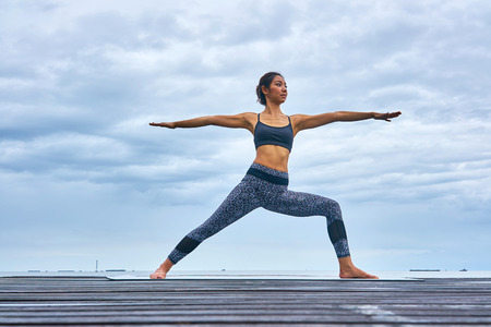 A woman professional trainer yoga pose on wooden bridge over seaside.の写真素材