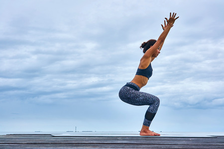 A woman professional trainer yoga pose on wooden bridge over seaside.の写真素材