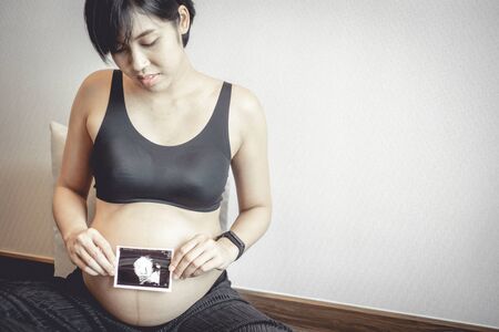 Close up of pregnant woman with ultrasound photo of her baby hold on her belly.の写真素材