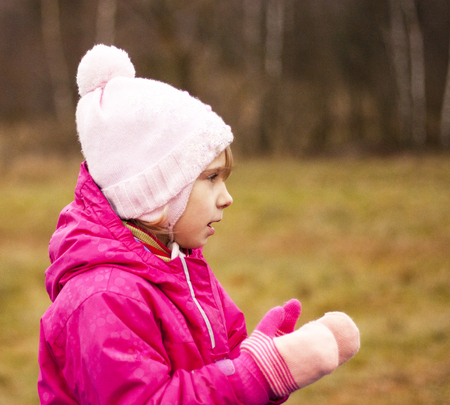 A child in a red jacket and white hat is playing on the street, clapping his hands in gloves. Autumn, close-upの写真素材