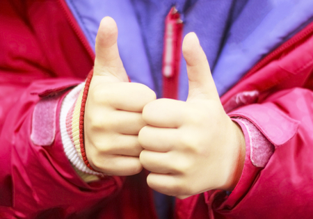 Young teenage girl giving thumb up on two hands as a sign of success. Concentrate on the hands.の写真素材