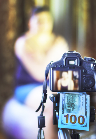 a camera, under it 100 dollars, in focus. in the background the girl does not focus. The concept of earning in a photo.の写真素材