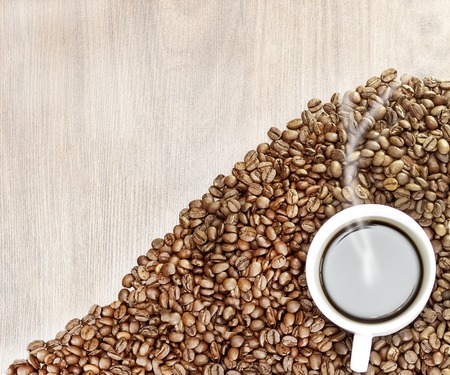 the heart of coffee beans on a wooden background in the center of a cup of white with coffee, with it comes steamの写真素材