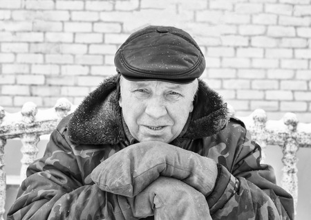 Winter. Cold. An elderly man leaned on a wooden stake. The jacket is dirty green, the mittens are also mud.の写真素材