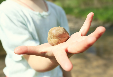 little girl holding a stone in her hand. The stone is a close-up. The girl does not focus.の写真素材