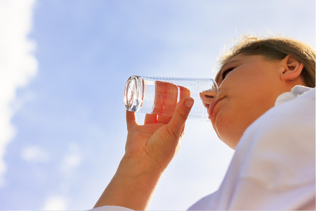 A woman is drinking water from a transparent glass in the street. Blue sky background.の写真素材