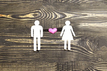 he and she are cut out of paper and in the middle a heart on a dark wooden background. illustration of the relationship between a devushka and a manの写真素材