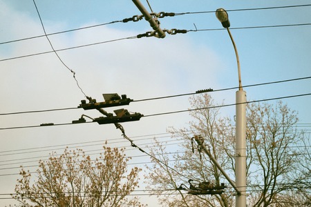 Trolley bus wires have a pillar against blue sky.