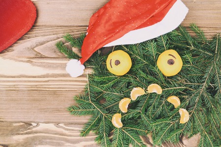 Christmas composition. Christmas pattern with tangerines, fir branch. The sad face of the branches of spruce and mandarin instead of eyes looking at us. have toning. and it's snowing. The red gift sock is emptyの写真素材