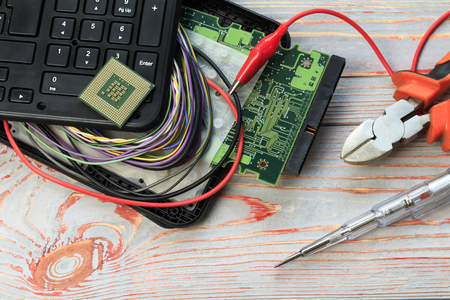 A broken laptop and a wire sticking out of it on it. There are side scissors and a screwdriver. repair technology concept. there is toningの写真素材