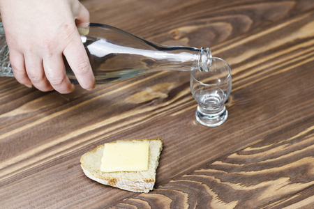 a glass of pure alcohol, a bottle and a piece of bread and cheese on a wooden background. a glass and on it a red cross. concept of quit drinking. there is toning.の写真素材
