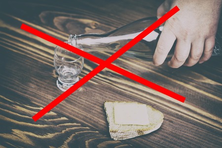 a glass of pure alcohol, a bottle and a piece of bread and cheese on a wooden background. a glass and on it a red cross. concept of quit drinking. there is toning.の写真素材