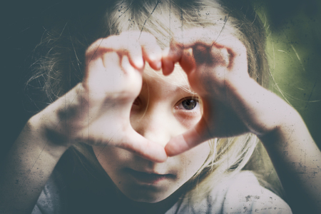 a girl with white hair makes a heart and looks into it. Concept view in childhood. there is toning.の写真素材