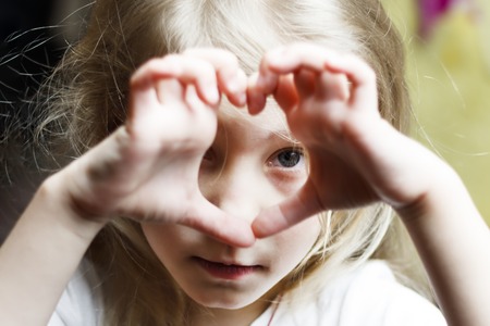 a girl with white hair makes a heart and looks into it. Concept view in childhood. there is toning.の写真素材