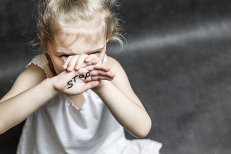 on a dark background, a child with his hands covers his face with a handwritten stop. Concept protect children from violence.の写真素材