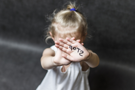 on a dark background, a child with his hands covers his face with a handwritten stop. Concept protect children from violence.の写真素材