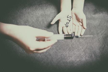 child's hand on the palm is written stop. the other holds a syringe with dark solutionsの写真素材