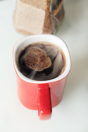 red mug. coffee is poured into it. He is a true steam. next to the glass jar, coffee granules are...