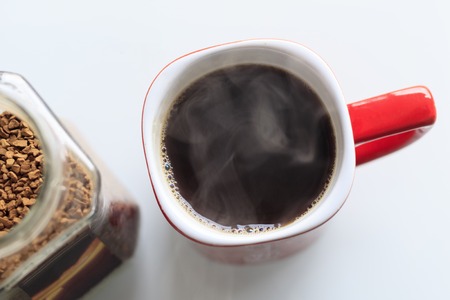 red mug. coffee is poured into it. He is a true steam. next to the glass jar, coffee granules are opened in it.の写真素材