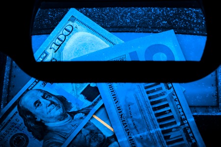 in the photo one hundred, fifty, five dollars. US banknotes. Equipment for in-depth inspection of money. Checking the bill in ultraviolet light. Fake money or financial crisis conceptの写真素材