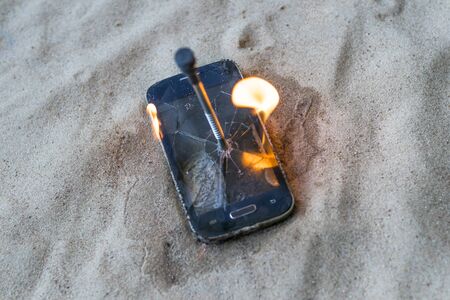 cellular telephone. on the beach sand. it has a metal nail in it. it burns with open fire.の写真素材