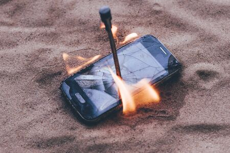 cellular telephone. on the beach sand. it has a metal nail in it. it burns with open fire.の写真素材