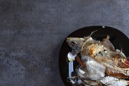 wooden background. a plate of dark color. there are bones from eaten fish